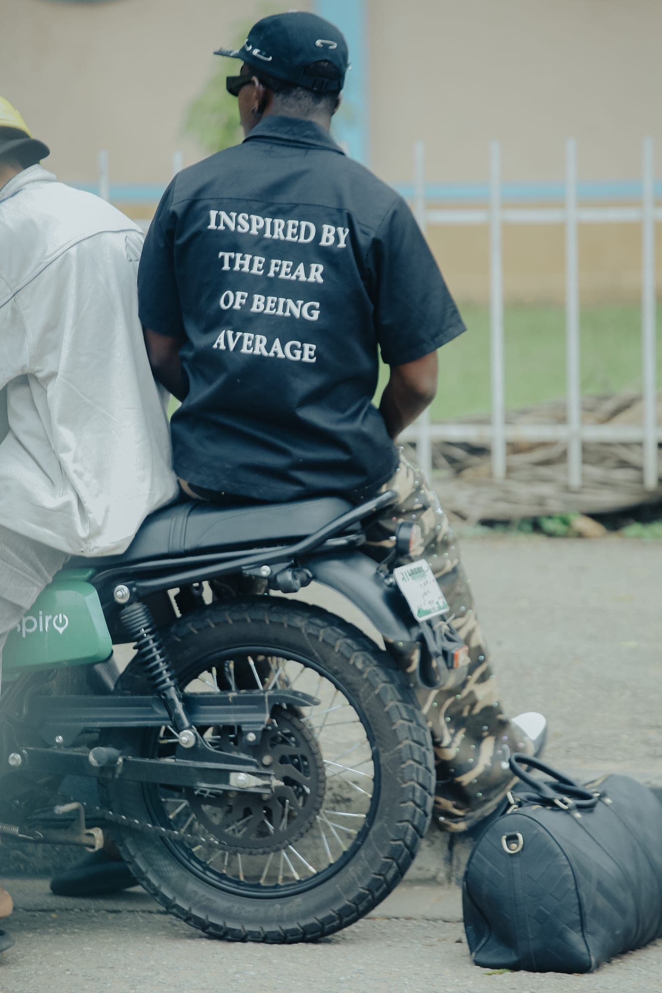 Back view of a shirt reading Inspired by the fear of being average, on a motorbike