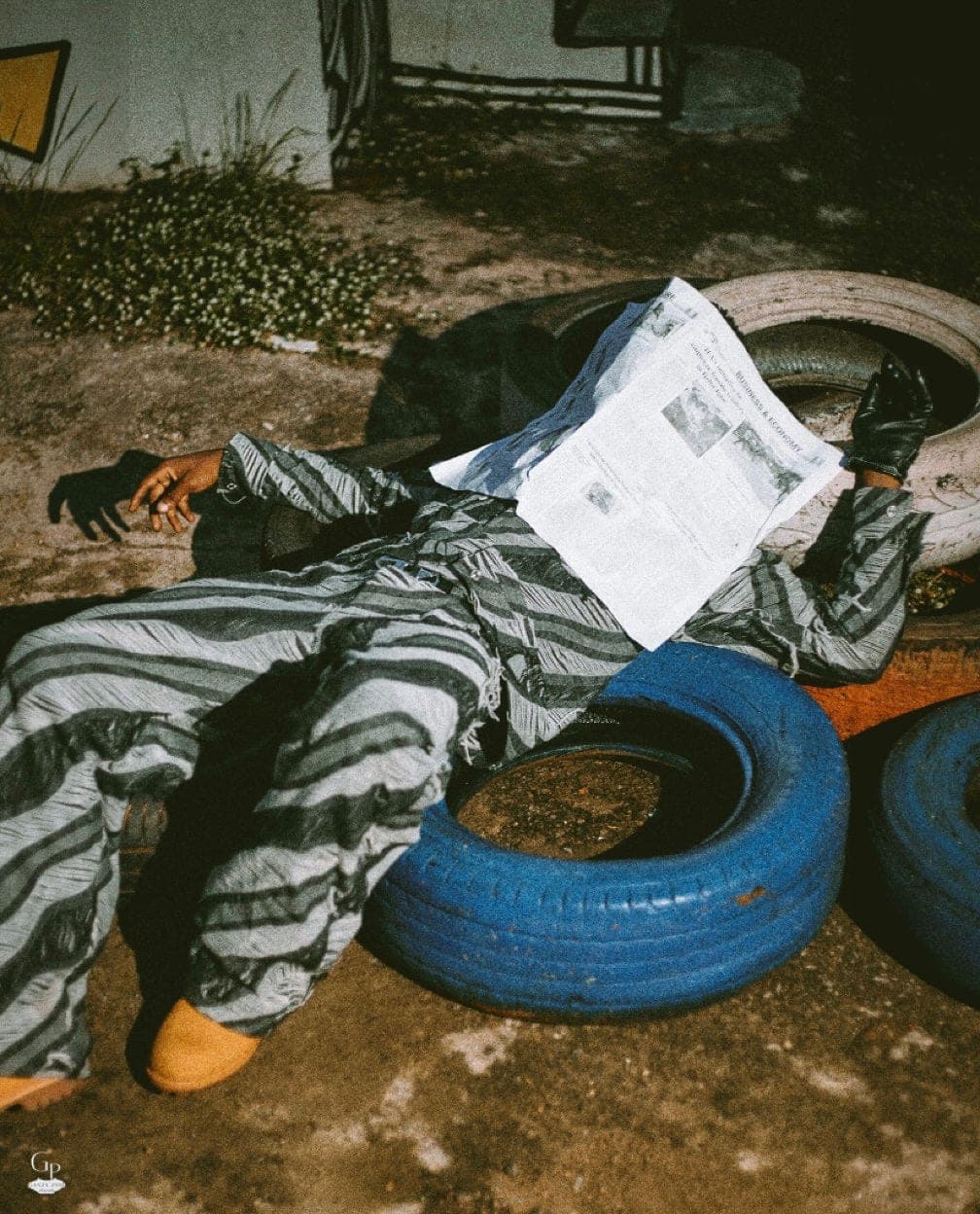 Lying across tyres in a striped set with a newspaper over the face