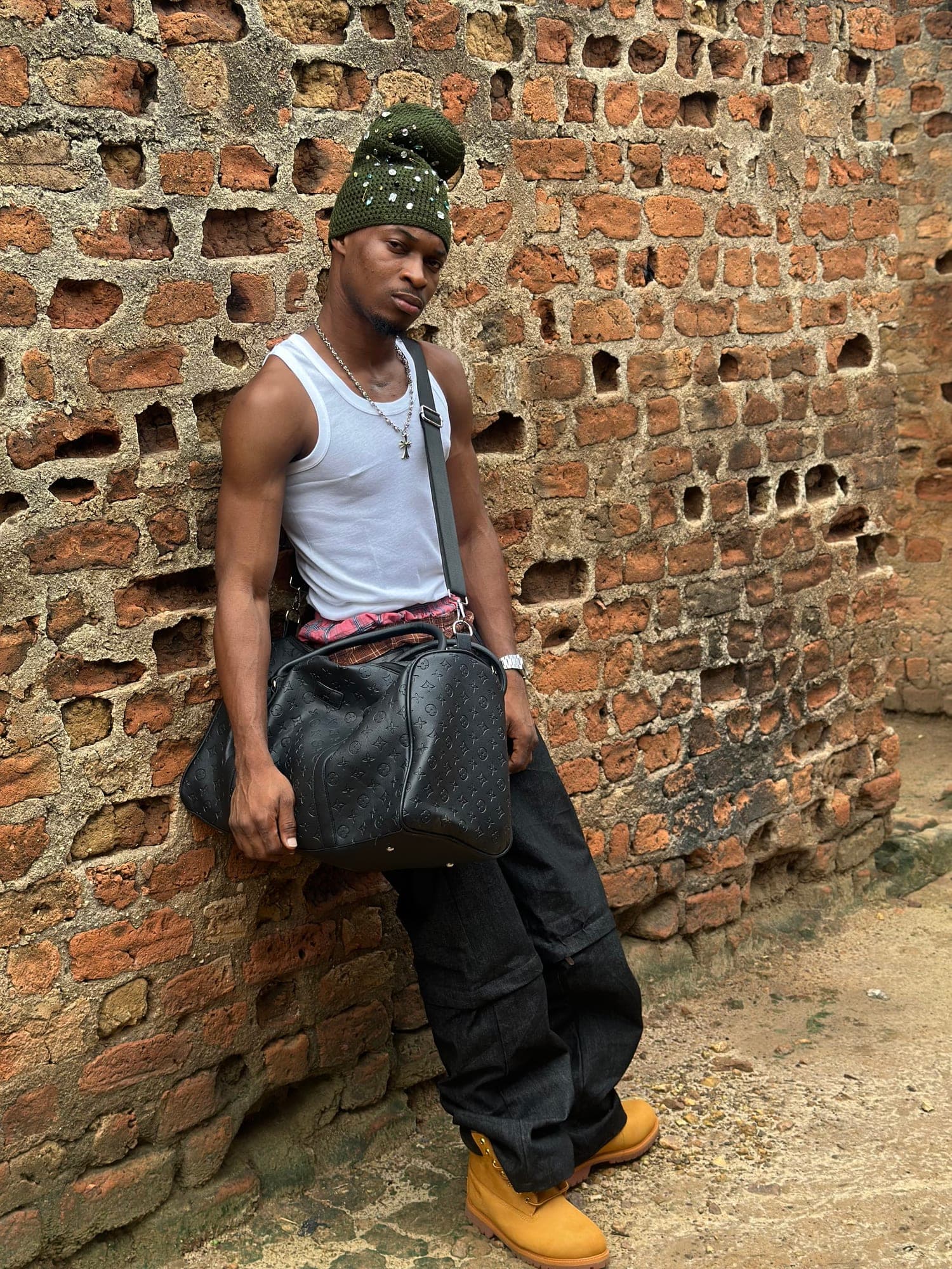 White tank, green beanie and black duffel against a brick wall