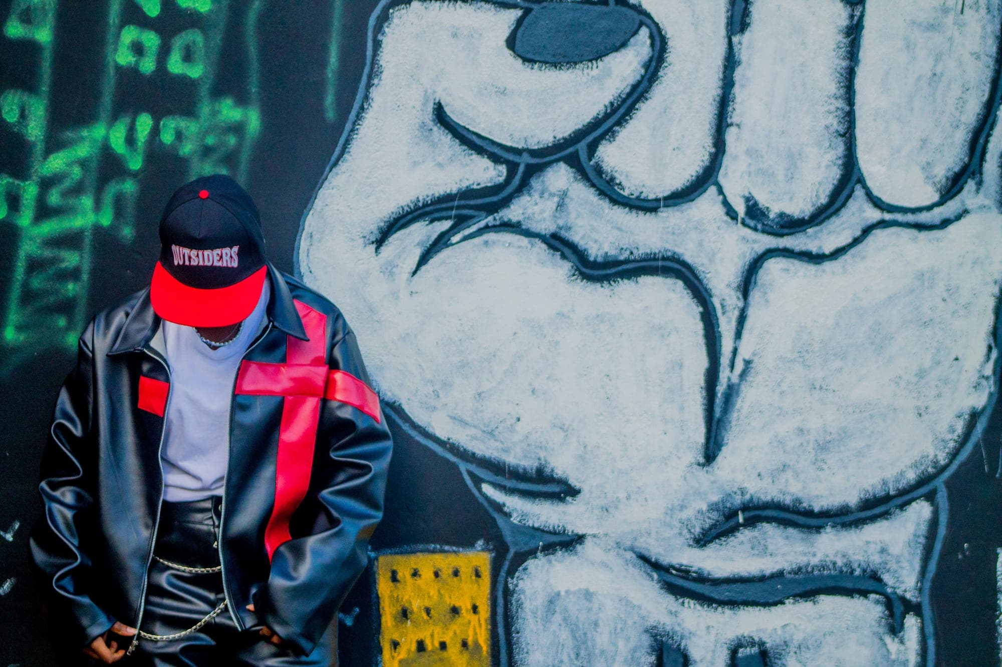 Leather jacket and red cap in front of a raised-fist mural
