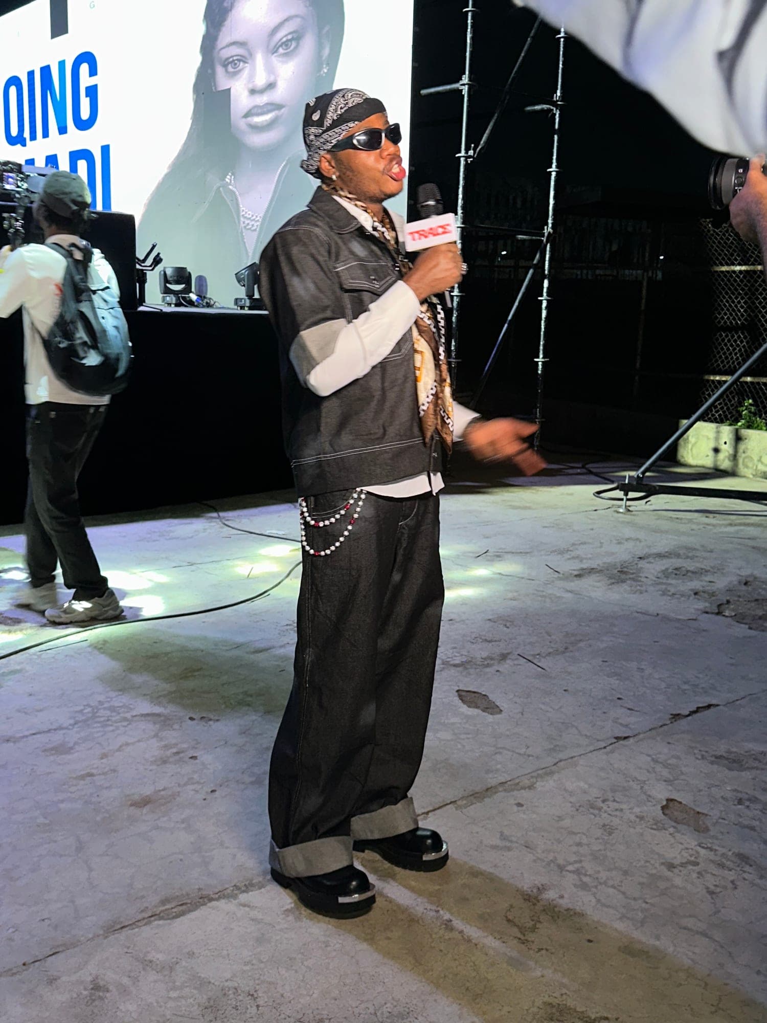 Host on stage in a leather vest, wide trousers and chains